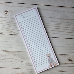 May include: A rectangular notepad with a pink border and the text "what a foxing busy day". The notepad features a watercolor illustration of a fox wearing a vest. The notepad has a lined section for a to-do list.