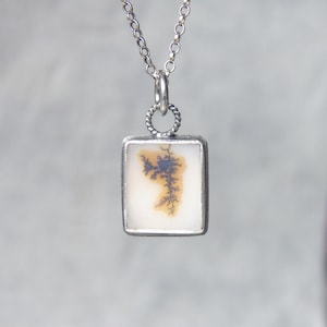 May include: A silver pendant necklace with a square-shaped agate stone featuring a dendritic pattern in shades of brown and white.