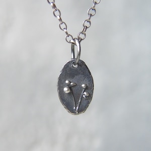 May include: A silver necklace with a small oval pendant featuring a delicate floral design. The pendant has a textured surface and two small silver flowers with rounded centres.