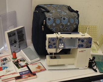 May include: A white sewing machine with a blue and gray patterned carrying case, a foot pedal, and various accessories including needles, bobbins, and instruction manuals.
