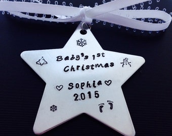 以下が含まれることがあります： 「Baby's 1st Christmas Sophia 2015」の文字と様々なクリスマスのシンボルが刻まれた、銀色の星型のクリスマスオーナメントです。