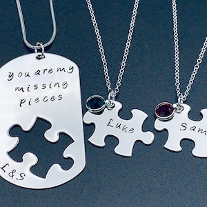 Puede incluir: Dos collares de plata con colgantes de pieza de rompecabezas. Un colgante tiene el texto "you are my missing pieces" y las iniciales "L&S". Los otros dos colgantes son más pequeños y tienen los nombres "Luke" y "Sam" grabados en ellos.