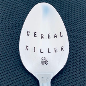 May include: A silver spoon with the words "CEREAL KILLER" engraved on it, along with a skull and crossbones symbol.