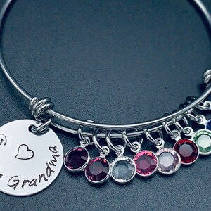 May include: A silver bangle bracelet with a charm that reads "Great Grandma" with a heart. The bracelet has multiple charms with colourful crystals.