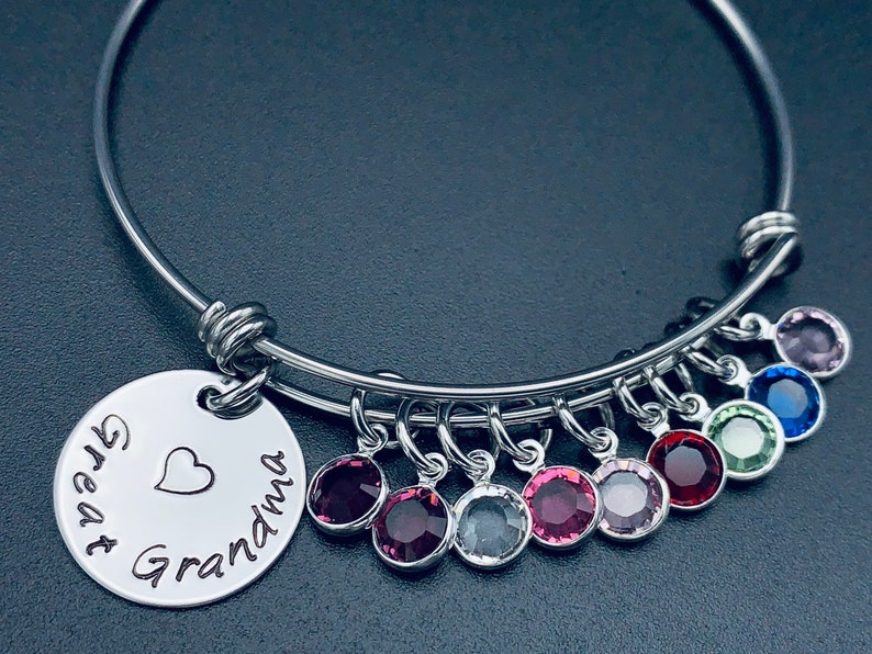 May include: A silver bangle bracelet with a charm that reads "Great Grandma" with a heart. The bracelet has multiple charms with colourful crystals.