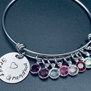 May include: A silver expandable bangle bracelet with a charm that reads "Great Grandma" with a heart. The bracelet has multiple charms with colourful crystals.