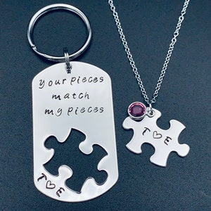 Może przedstawiać: Srebrny brelok do kluczy i naszyjnik w kształcie puzzli. Brelok ma napis "your pieces match my pieces", a naszyjnik ma mały fioletowy kamień szlachetny. Oba elementy mają wygrawerowany napis "T❤E".