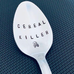 May include: A silver spoon with the words "CEREAL KILLER" engraved on it, along with a small skull and crossbones symbol.