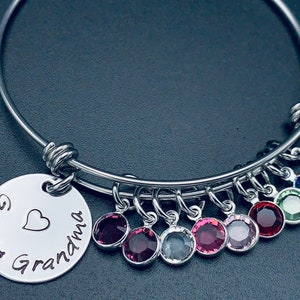 May include: A silver bangle bracelet with a charm that reads "Great Grandma" with a heart. The bracelet has multiple charms with colourful crystals.