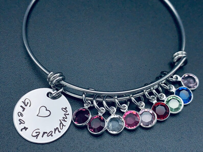 May include: A silver bangle bracelet with a charm that reads "Great Grandma" with a heart. The bracelet has multiple charms with colourful crystals.