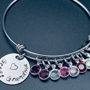 May include: A silver bangle bracelet with a charm that reads "Great Grandma" with a heart. The bracelet has multiple dangling charms with colourful crystals.