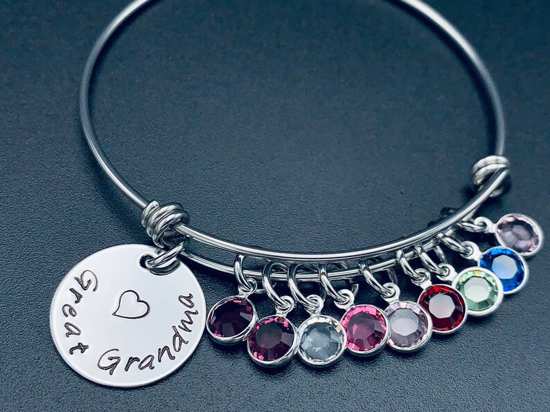 May include: A silver bangle bracelet with a charm that reads "Great Grandma" with a heart. The bracelet has multiple dangling charms with colourful crystals.