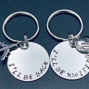May include: Two silver keychains with round tags. One tag has a small airplane charm and the text "I'll be back". The other tag has a small globe charm and the text "I'll be waiting".