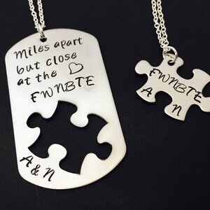 May include: Two silver necklaces with matching puzzle pieces. One necklace has a dog tag pendant with the text "Miles apart but close at the heart FWNBTF" and the other necklace has a puzzle piece pendant with the text "FWNBTF A & N".