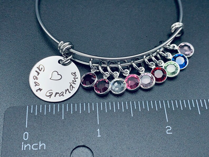 May include: A silver bangle bracelet with a charm that reads "Great Grandma" with a heart. The bracelet has multiple charms with colourful crystals.