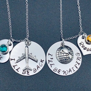 May include: Two silver necklaces with heart pendants and round charms. One necklace has a charm with a plane and the text "I'll be back". The other necklace has a charm with a globe and the text "I'll be waiting".