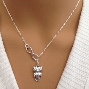 May include: A silver necklace with an infinity symbol charm and an owl pendant. The owl has a detailed design with small flowers on its wings.