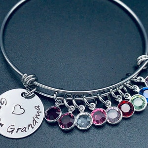 May include: A silver bangle bracelet with a charm that reads "Great Grandma" with a heart. The bracelet has eight dangling charms with colourful crystals.