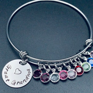May include: A silver bangle bracelet with a charm that reads "Great Grandma" with a heart. The bracelet has nine dangling charms with colourful crystals.