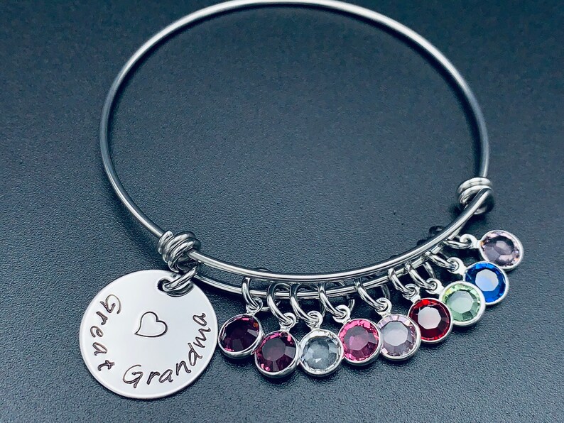 May include: A silver bangle bracelet with a charm that reads "Great Grandma" with a heart. The bracelet has nine dangling charms with colourful crystals.