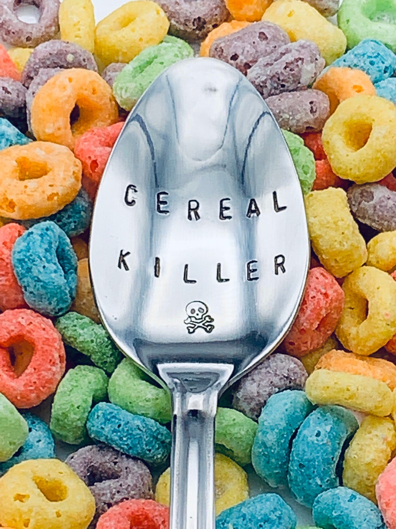 May include: A silver spoon with the words "Cereal Killer" engraved on it, surrounded by colorful cereal rings.