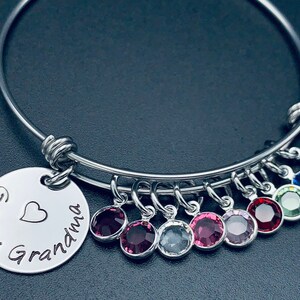 May include: A silver bangle bracelet with a charm that reads "Great Grandma" with a heart. The bracelet has multiple charms with colourful crystals.