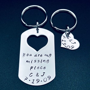 May include: A silver keychain set with two heart-shaped tags. One tag says "you are my missing piece C & J 7.19.09" and the other tag says "C & J 7.19.09".