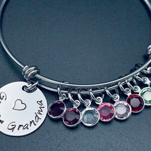 May include: A silver bangle bracelet with a charm that reads "Great Grandma" with a heart. The bracelet has multiple charms with colourful crystals.