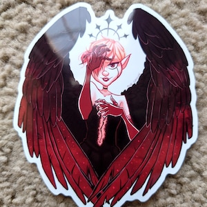 Puede incluir: Una pegatina con una ilustración estilizada de una figura con alas rojas oscuras y negras. La figura tiene la piel pálida, el pelo rojo y lleva un atuendo negro. Las alas están extendidas y la pegatina tiene un borde blanco.