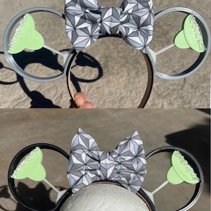 May include: A pair of mouse ears with a geometric patterned bow in shades of gray and white. The ears are designed with margarita glasses in light green with a rim of white crystals. The headband is black and brown.