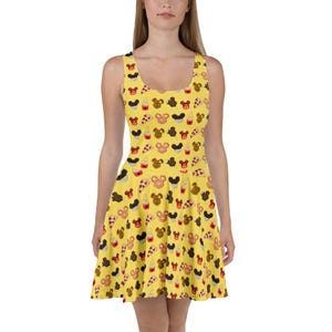 May include: A yellow sleeveless dress with a repeating pattern of Mickey Mouse-shaped treats. The dress features a scoop neckline and a flared skirt. The pattern includes ice cream cones and cupcakes. The dress is a fun and whimsical design.