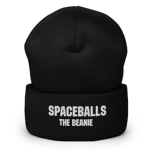 Puede incluir: Gorro negro con el texto "SPACEBALLS THE BEANIE" en letras blancas. El gorro está hecho de un material suave y tejido y está diseñado para ser usado en la cabeza.
