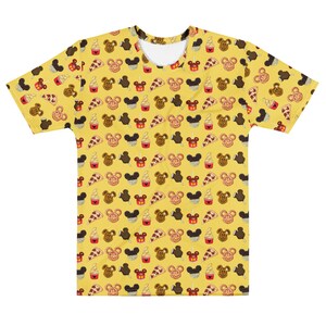 May include: Yellow t-shirt featuring a repeating pattern of Mickey Mouse-shaped ice cream, pretzels, pizza slices, and ice cream cones. The shirt has a crew neck and short sleeves. The design is in brown, black, red, and white.