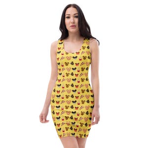 May include: A yellow bodycon dress with a repeating pattern of cartoon character faces and desserts. The sleeveless dress has a scoop neckline and is form-fitting. The pattern includes images of cupcakes, ice cream, and pizza.