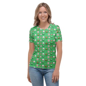 May include: A green women's t-shirt with a repeating pattern of golf-themed icons, including golf balls, golf clubs, flags, and a golf cart. The icons are in shades of red, white, and blue.