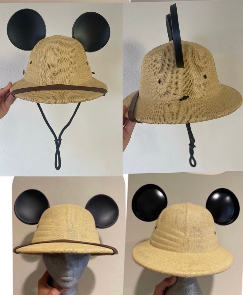 May include: A tan safari hat with black Mickey Mouse ears attached. The hat has a brown leather band around the brim and a black chin strap.