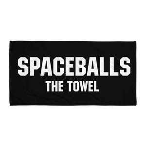 May include: Black rectangular beach towel with the text "SPACEBALLS THE TOWEL" in large white block letters. The towel is a solid black color, and the text is centered on the towel.