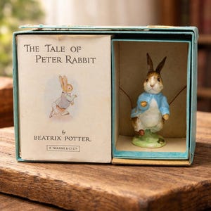 May include: A boxed figurine of Peter Rabbit from "The Tale of Peter Rabbit" by Beatrix Potter. The figurine is in a blue box with the book cover art. The rabbit wears a blue jacket and stands on a green base.