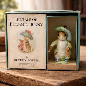 May include: A boxed figurine of Benjamin Bunny from "The Tale of Benjamin Bunny" by Beatrix Potter. The figurine is wearing a green hat and jacket, holding a carrot. The box has the book title and author's name.