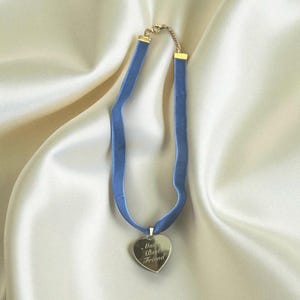 May include: A blue velvet choker necklace with a heart-shaped pendant. The pendant is engraved with the words "Man Best Friend". The necklace has a gold-colored clasp and chain.
