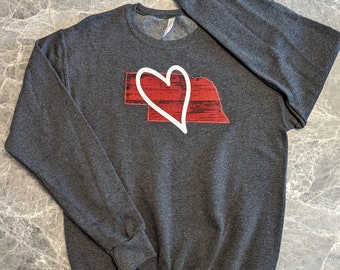 May include: A dark gray sweatshirt with a red and white graphic of the state of Nebraska with a white heart over it.
