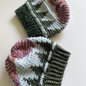 Pu&ograve; includere: Due berretti all'uncinetto con un motivo verde, bianco e multicolore. I berretti sono realizzati con un filato spesso e hanno un bordo a coste.