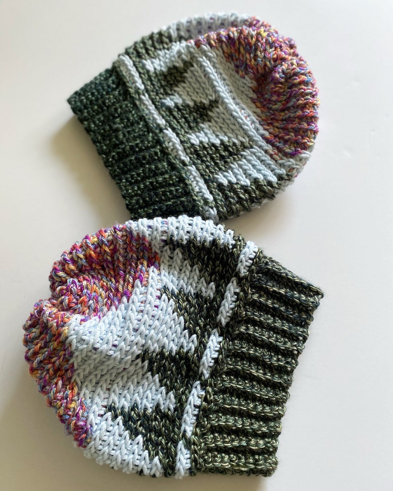 Pu&ograve; includere: Due berretti all'uncinetto con un motivo verde, bianco e multicolore. I berretti sono realizzati con un filato spesso e hanno un bordo a coste.
