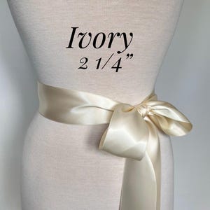 May include: Ivory satin sash tied in a bow, 2 1/4 inches wide, draped around a mannequin. The text "Ivory" and "2 1/4"" is printed on the mannequin.