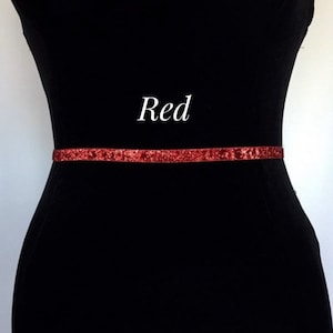 May include: A red glitter belt on a black dress form. The belt is thin and has a subtle sparkle. The word "Red" is written in white text above the belt.