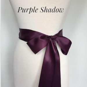 May include: A purple satin ribbon tied in a bow around a white dress form. The text "Purple Shadow" is written above the ribbon.