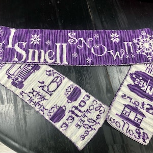 May include: A purple and white knitted scarf with the text "I Smell Snow" and winter-themed designs.