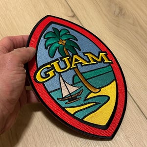 May include: A red, yellow, green, and blue embroidered patch with the word "GUAM" in yellow letters and a palm tree and sailboat on a beach.
