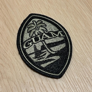 May include: A green and black embroidered patch with the word "GUAM" and a palm tree on a beach.