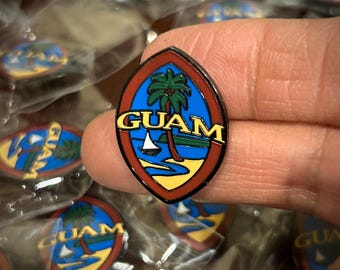 May include: A red, yellow, and blue enamel pin with a palm tree and the word "GUAM" in white letters. The pin is shaped like the outline of the island of Guam.